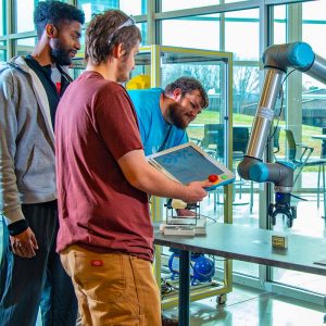 Photo of 3 WPCC students working with a robot claw picking up blocks in the Mechatronics Lab
