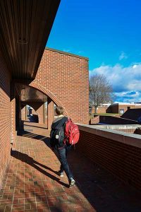 Photo of a student carrying a backpack waling away from the camera at the side of Phifer Hall