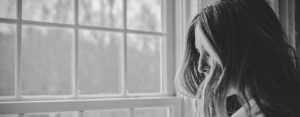 Photo of the silhouette of a woman looking out a window