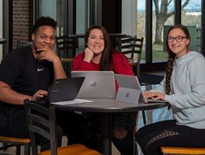 Three smiling WPCC students pose while doing homework in Jim Burnett Hall's lounge area.
