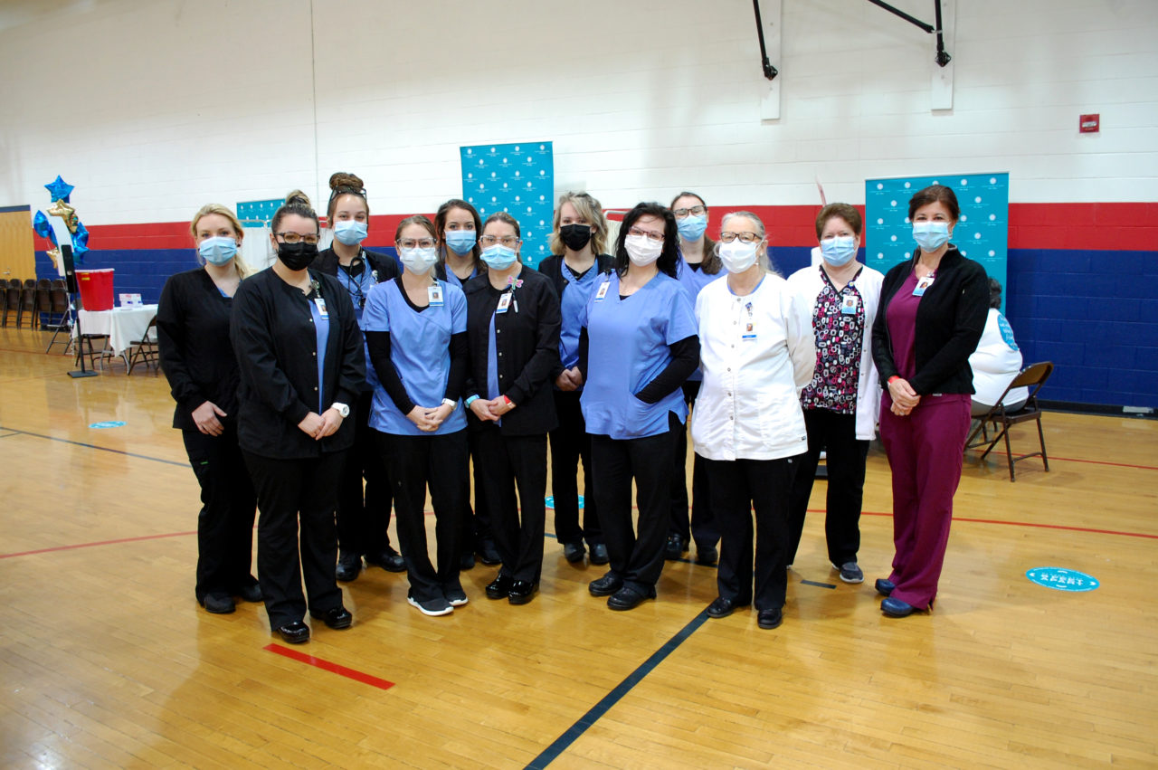 Nursing students and instructors pose in the Freedom High School vaccine clinic, wearing scrubs and masks.