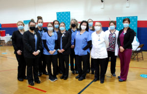 Nursing students and instructors pose in the Freedom High School vaccine clinic, wearing scrubs and masks.