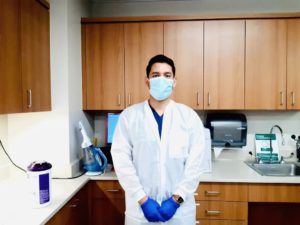 Noe Lopez in the lab wearing gloves, lab coat and mask.