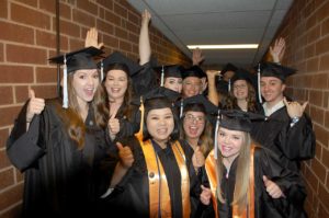 A group of happy graduates celebrate with thumbs up and high-fives