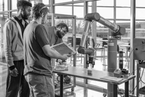 Three WPCC students work with a robotic arm in class