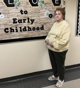 Image of older female student standing in front of early childhood bulletin board
