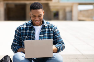 Image of a male student smiling while typing on a laptop