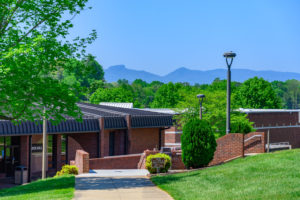 Image of phifer hall on wpcc campus during summer with bright green trees and grass with table rock outline in the distance