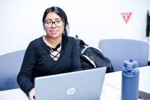 Image of female student smiling with a laptop and water bottle.