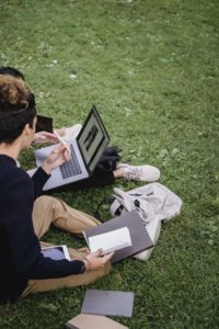 Image of students working outside on grass with a laptop and notebook