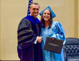 Image of an adult high school with their diploma smiling for a photo with dr.welch wpcc president