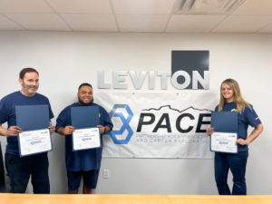 Image of 3 apprentices holding their certificate smiling for a photo in front of a PACE banner