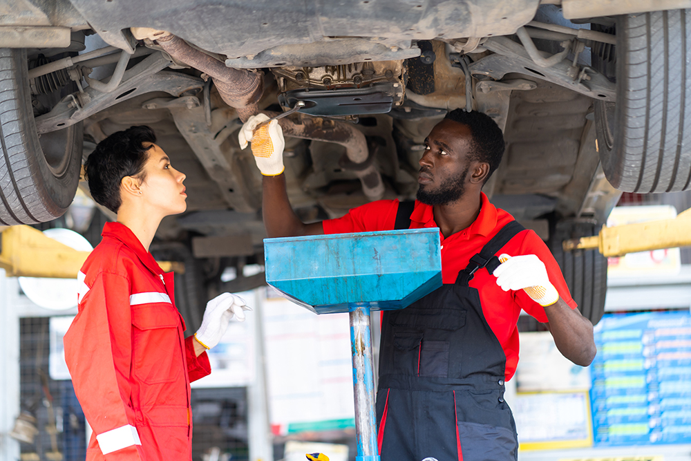 Male And Female trainee Mechanics Working Underneath Car