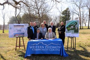 Image of 8 people in front of a western piedmont community college table for a signing with a poster on each side.