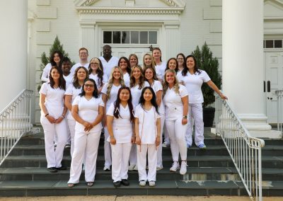 Image of nursing students standing on stairs in white scrubs smiling for a photo.