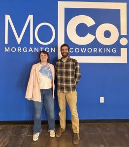 Image of 2 people smiling for a photo in front of the MoCo logo.