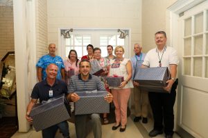 10 people smiling for a photo holding gift boxes.