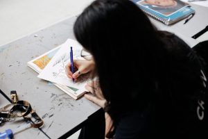 Female student holding a pencil sketching an image on a sketchpad.