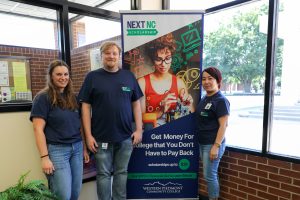 3 financial aid counselors in front of a stand up banner