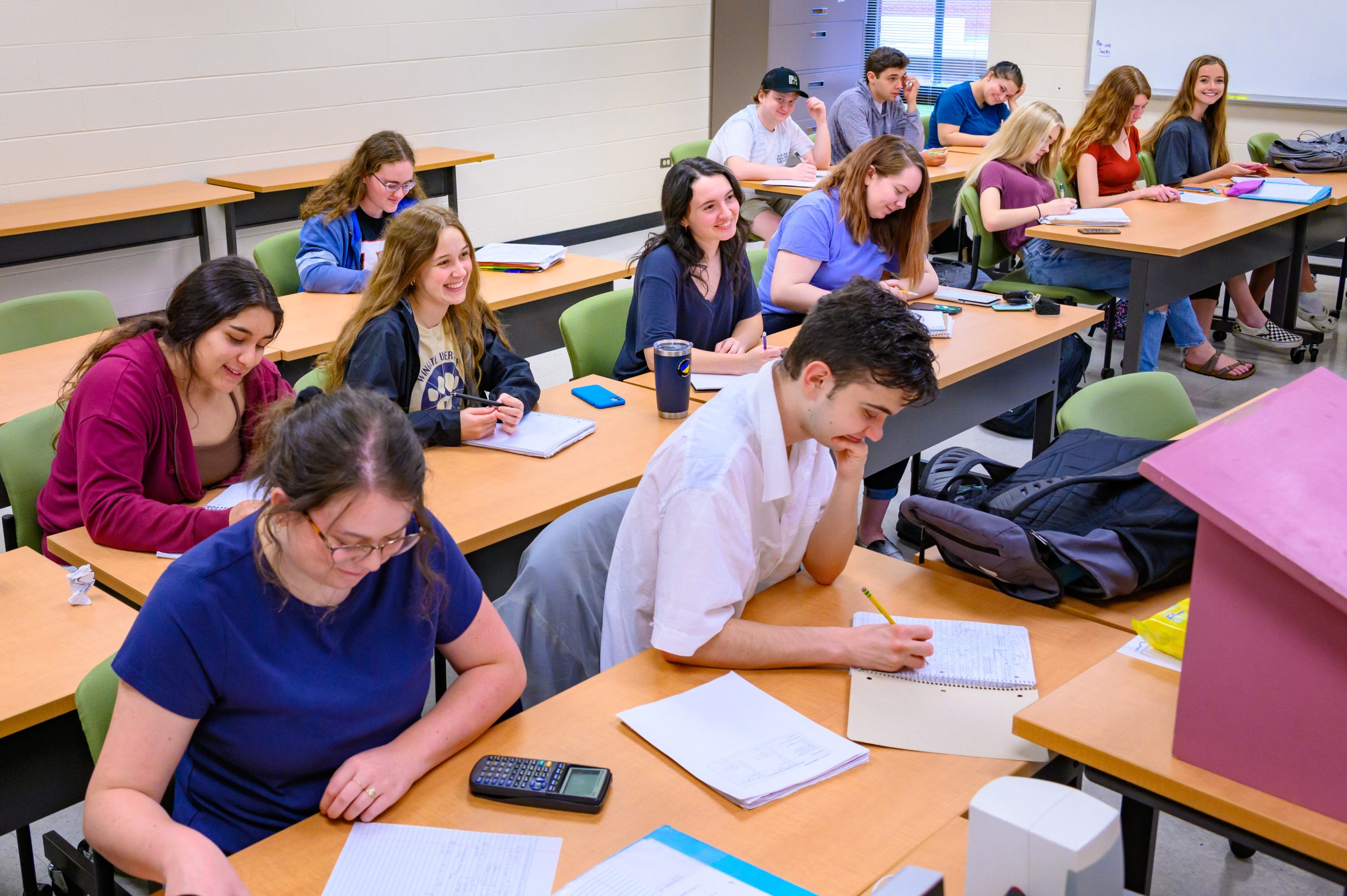 Three rows of students sitting at tables in a classroom looking down and forward. 