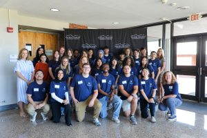 Image of students and staff at a pharmacy camp smiling for a photo in front of a black wpcc backdrop.
